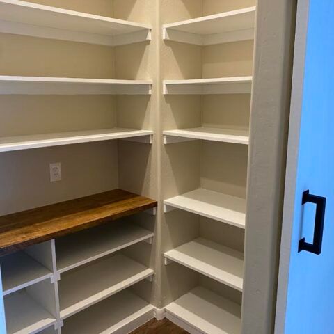 Walk-in closet with white shelving, cubbies, and a wood countertop