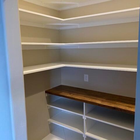 Walk-in closet with beige walls, white shelves, and a dark wood hanging rod