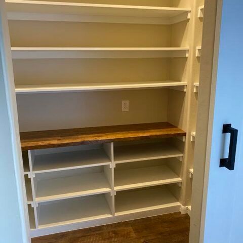 Built-in white closet shelves with a wood countertop and open cubbies, viewed through a doorway.