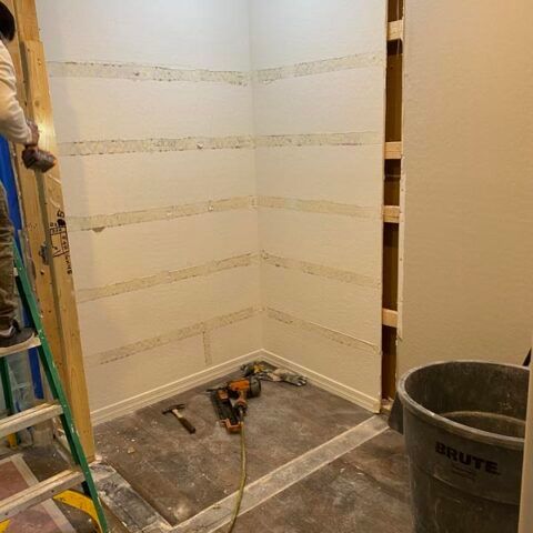 Bathroom under renovation with tiled shower walls, tools on the floor, ladder, and a bucket