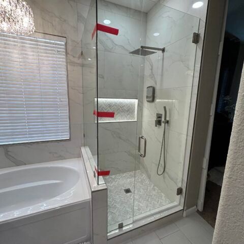 Modern bathroom with a glass walk-in shower, soaking tub, and white marble tile, lit by recessed lights