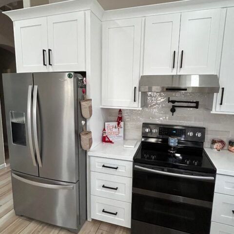 Modern white kitchen with stainless steel refrigerator, black stove, and white cabinets