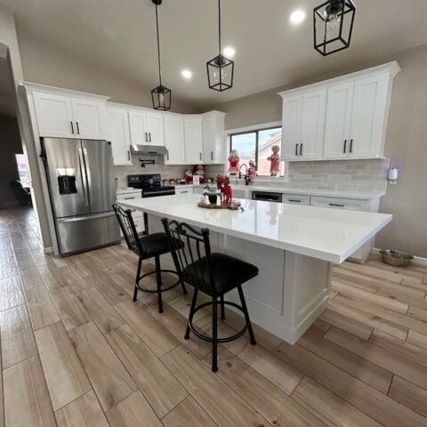 Bright modern kitchen with white cabinets, stainless steel fridge, large island, and black bar stools