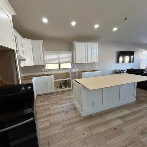 Bright modern kitchen with white cabinets, large island, tiled floor, and black appliances