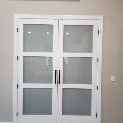 White double glass doors with black handles in a beige hallway