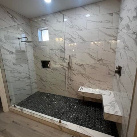 Modern tiled shower with black mosaic floor, marble-look walls, bench, and small windows