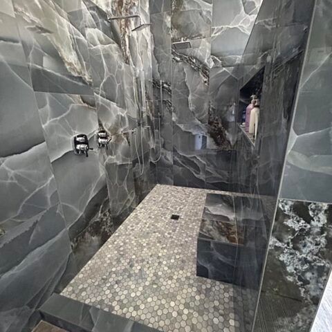 Modern gray tiled walk-in shower with mosaic floor and built-in shelf