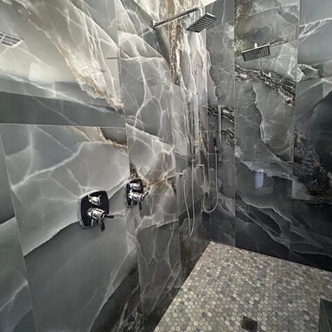 Modern bathroom with gray stone walls, chrome shower controls, and a mosaic tile floor.