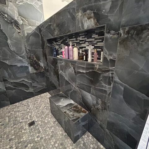 Dark marble-tiled shower with a built-in shelf holding toiletries and a small bench seat.