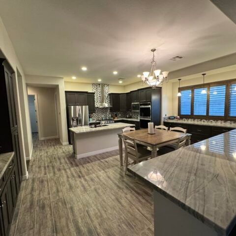 Modern kitchen and dining area with dark cabinets, marble countertops, island, and chandelier lighting