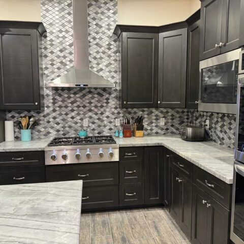 Modern kitchen with dark cabinets, stainless steel appliances, mosaic backsplash, and marble-look countertops