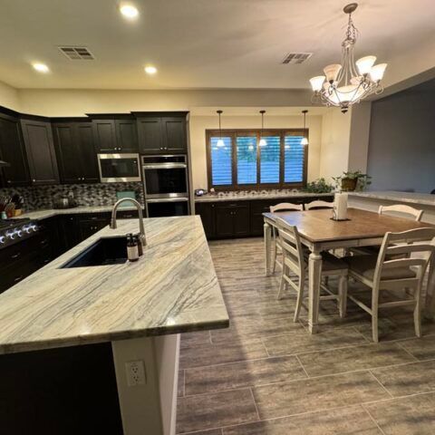 Modern kitchen with dark cabinets, large island, dining table, and window over the sink