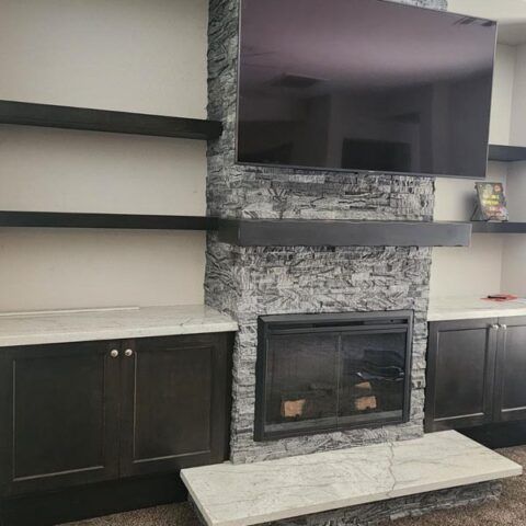 Modern living room with stone fireplace, wall-mounted TV, dark cabinets, and a light bench fireplace hearth