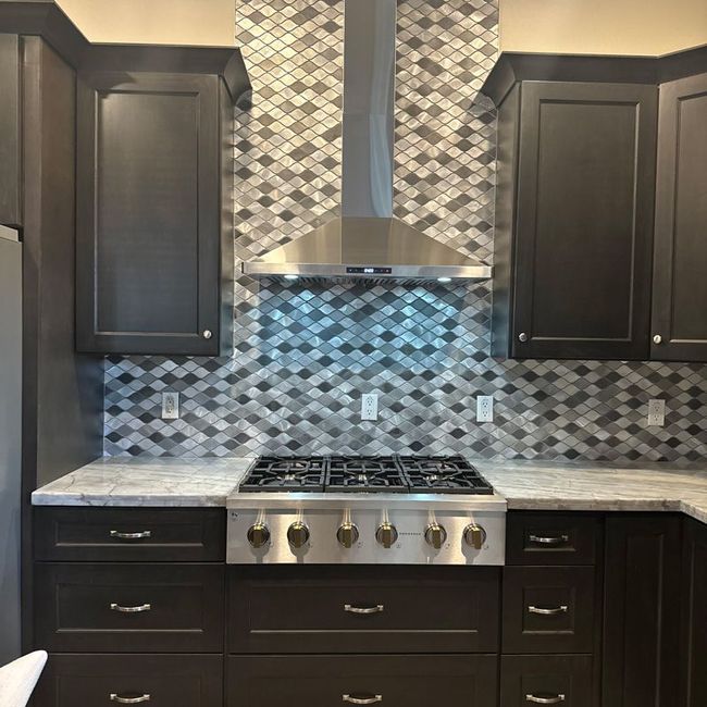 Modern kitchen with dark wood cabinets, stainless range hood, and gray-blue mosaic tile backsplash