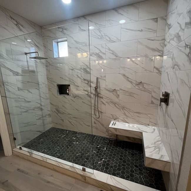 Tiled walk-in shower with marble-look walls, black pebble floor, bench, and two small windows.