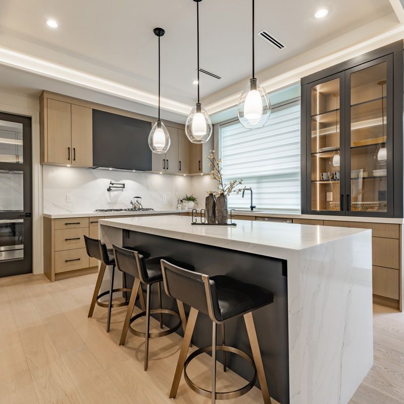 Modern kitchen with white island, black stools, pendant lights, and wood cabinetry