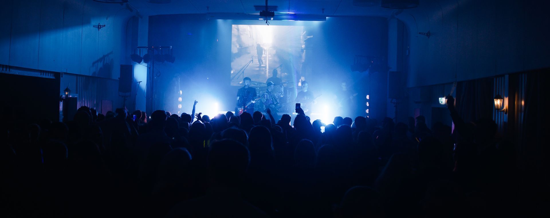 Band opptrer på scenen, badet i blått lys. Publikum med hendene i været.