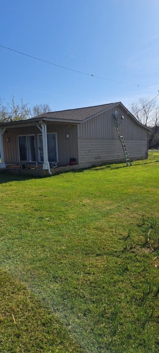 Small light-colored house with a front porch in a sunny yard under a blue sky