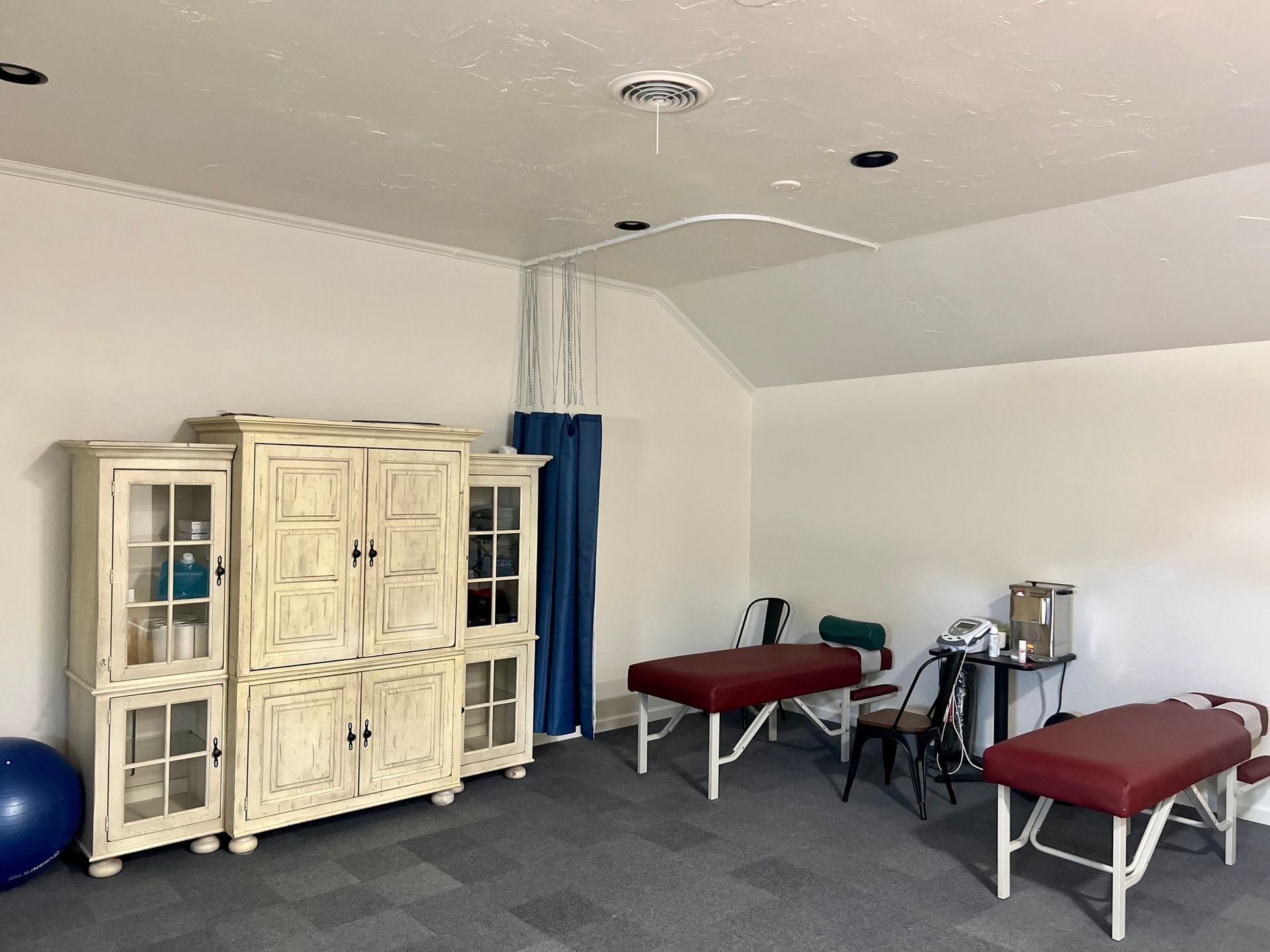 Sparse therapy room with massage table, red cot, cabinet, and blue exercise ball