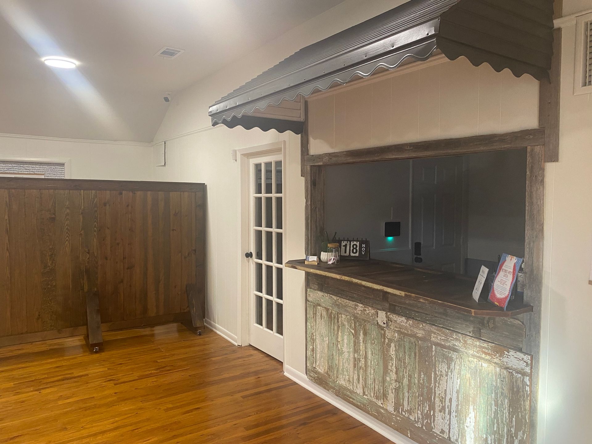 Empty bar area with wood floor, dark counter, and white French door under a striped awning.