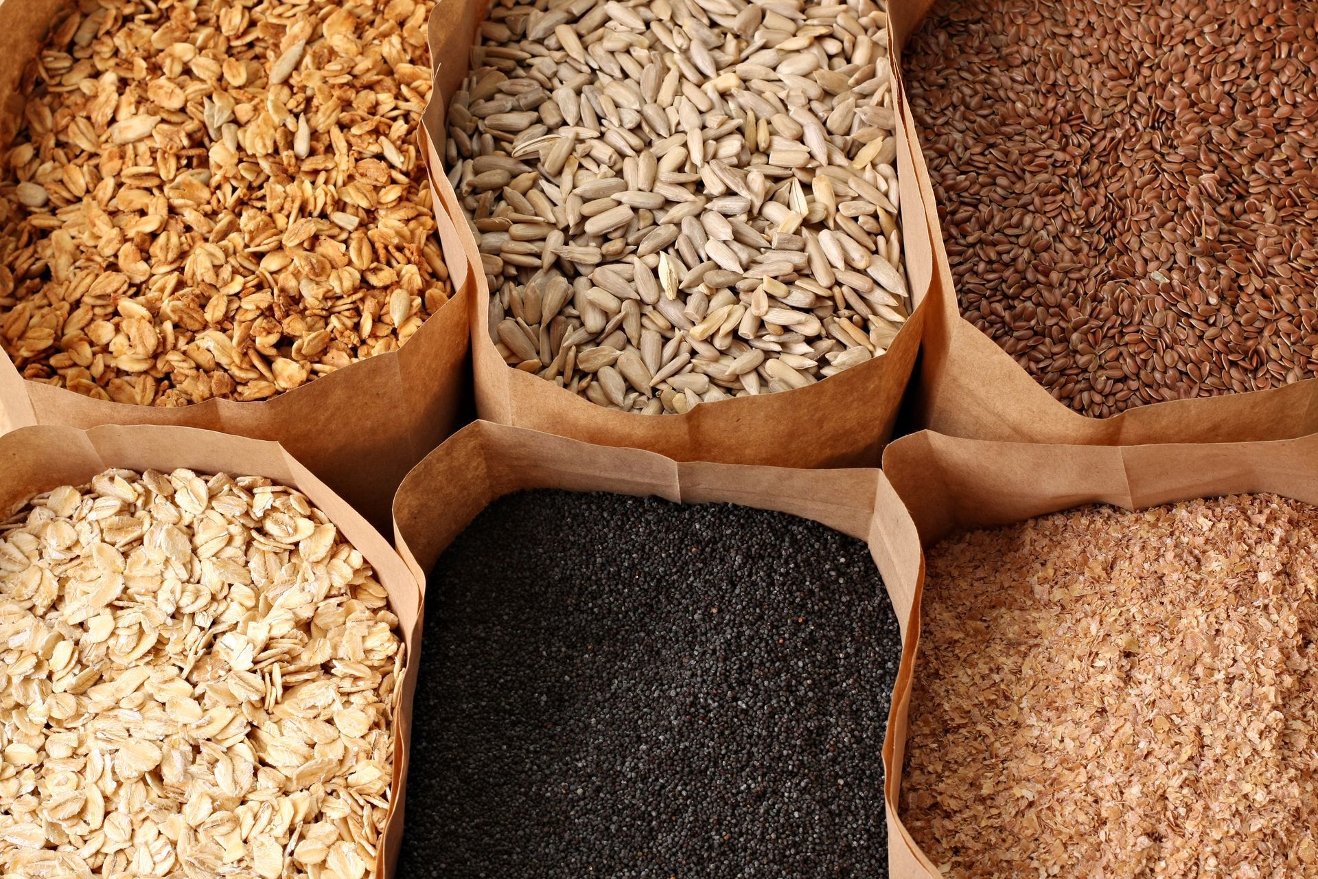 Six paper bags filled with assorted grains and seeds, viewed from above.