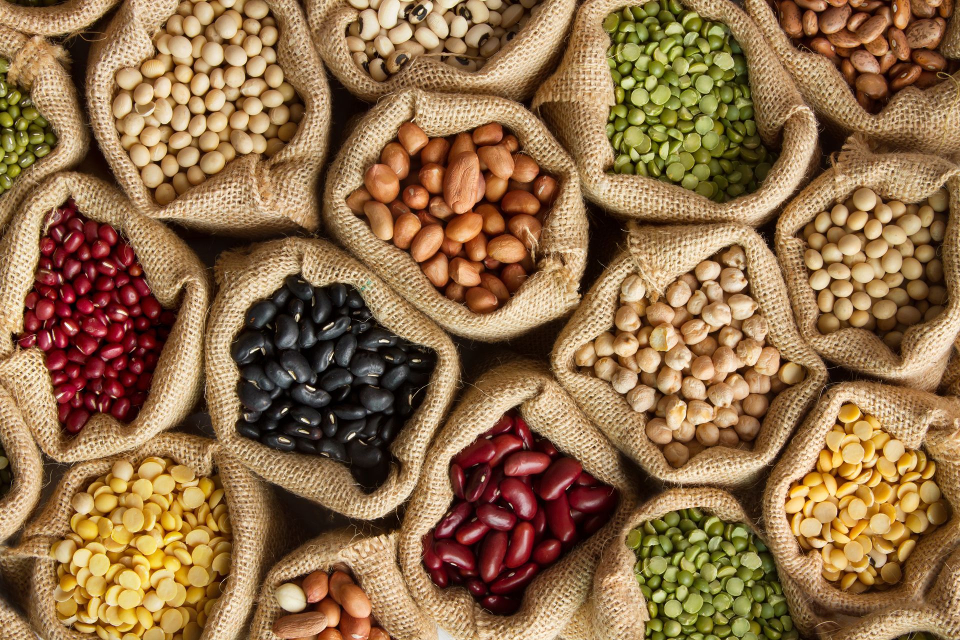 Assorted colorful beans and grains in burlap sacks arranged in a market display