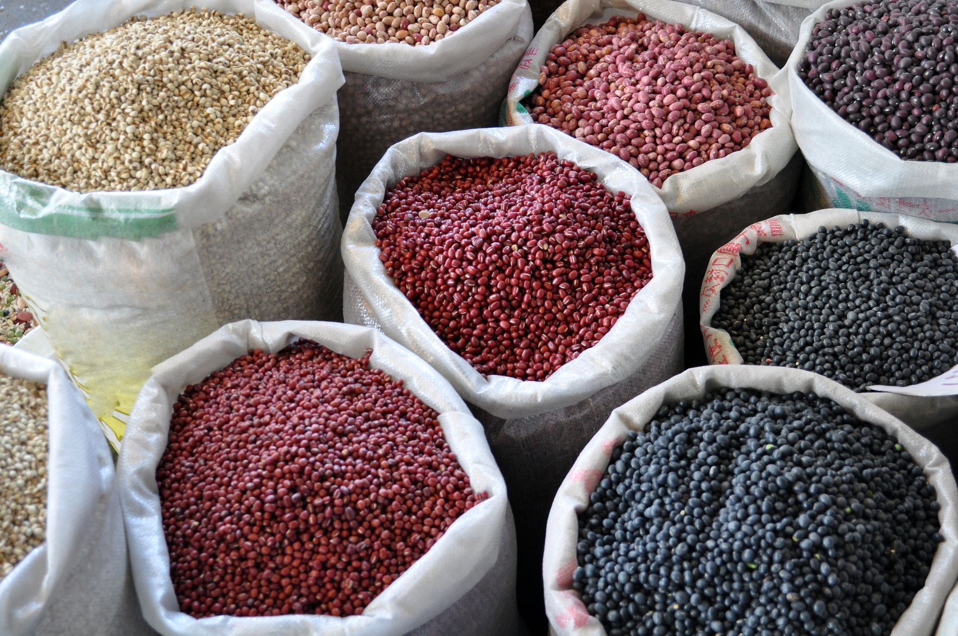 Sacks of assorted dried beans in red, black, and beige, displayed in a market stall