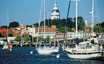 Sailboats in a harbor with waterfront buildings and a church tower in the background.