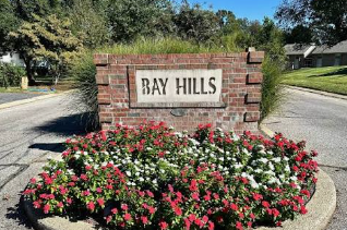 Brick entrance sign reading “Bay Hills” surrounded by red and pink flowers