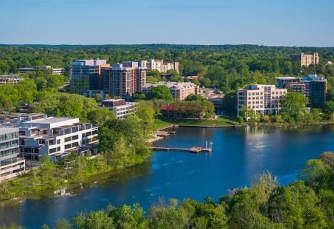 Lakefront apartment buildings beside a calm blue lake with trees and a dock Lakefront apartment buildings beside a calm blue lake with trees and a dock