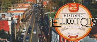 Historic Ellicott City sign over a downtown street with buildings and cars Historic Ellicott City sign over a downtown street with buildings and cars