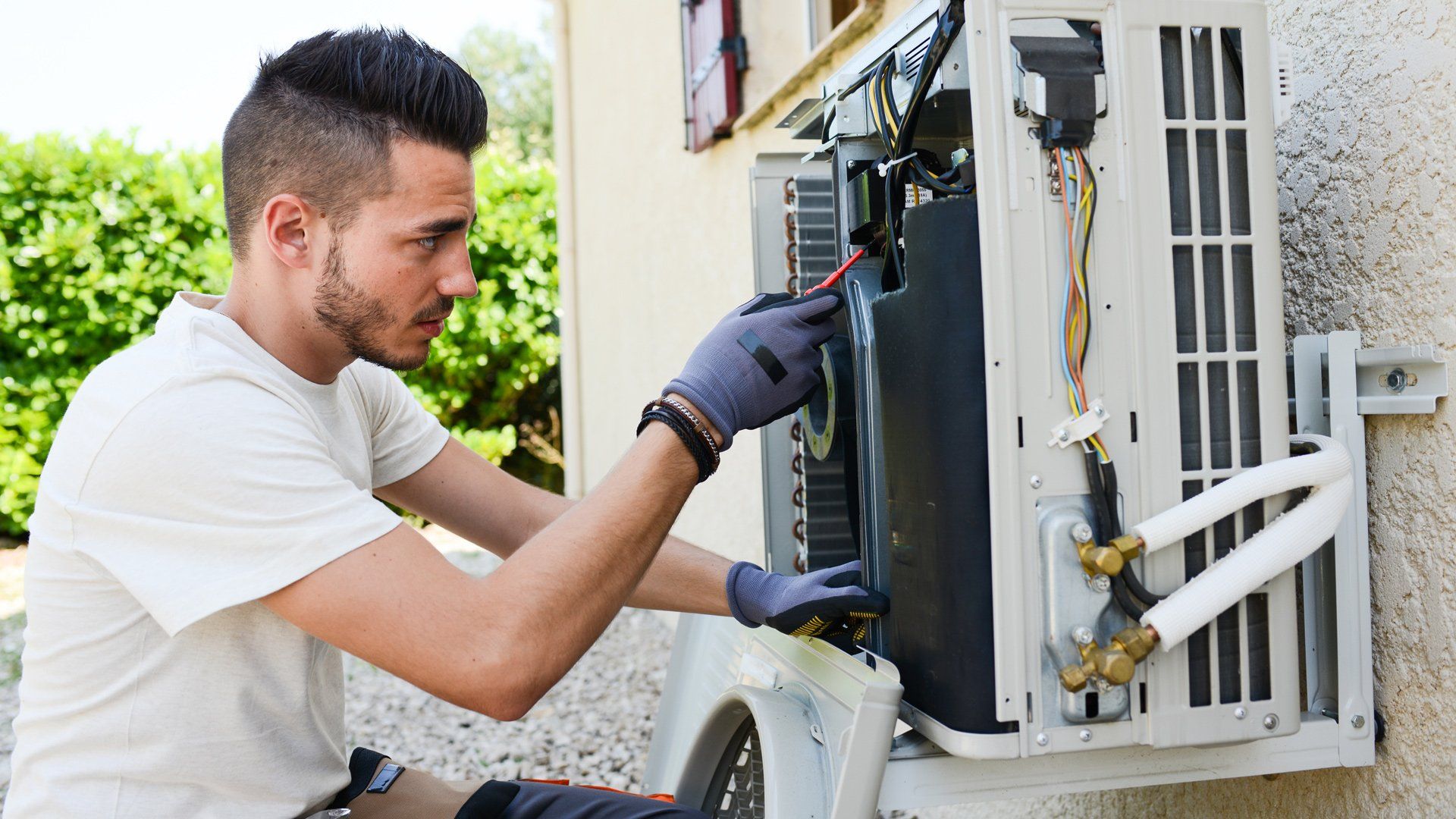Technician inspecting an outdoor air conditioner unit with tools outside a house Technician inspecting an outdoor air conditioner unit with tools outside a house