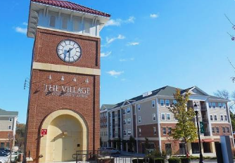 Brick clock tower with a red-tiled roof at Publix Village, beside modern apartment buildings under a blue sky