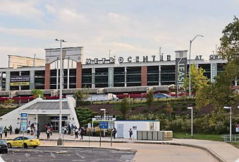 Outdoor view of a modern transit station with pedestrians, taxis, and a raised walkway at dusk