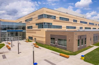 Modern tan office building with glass entrance and courtyard under a cloudy sky