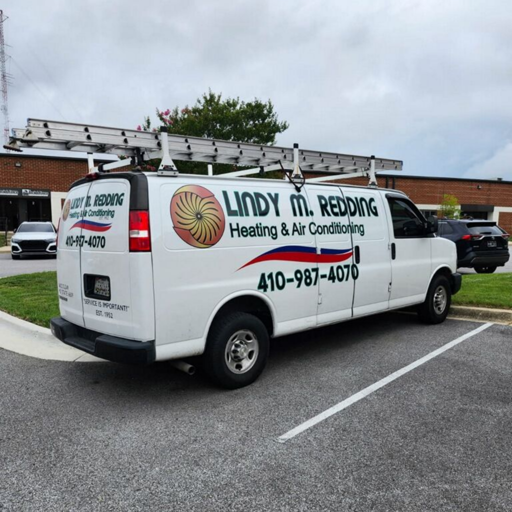 White heating and air conditioning service van with ladders parked in a lot, logo and phone number on the side