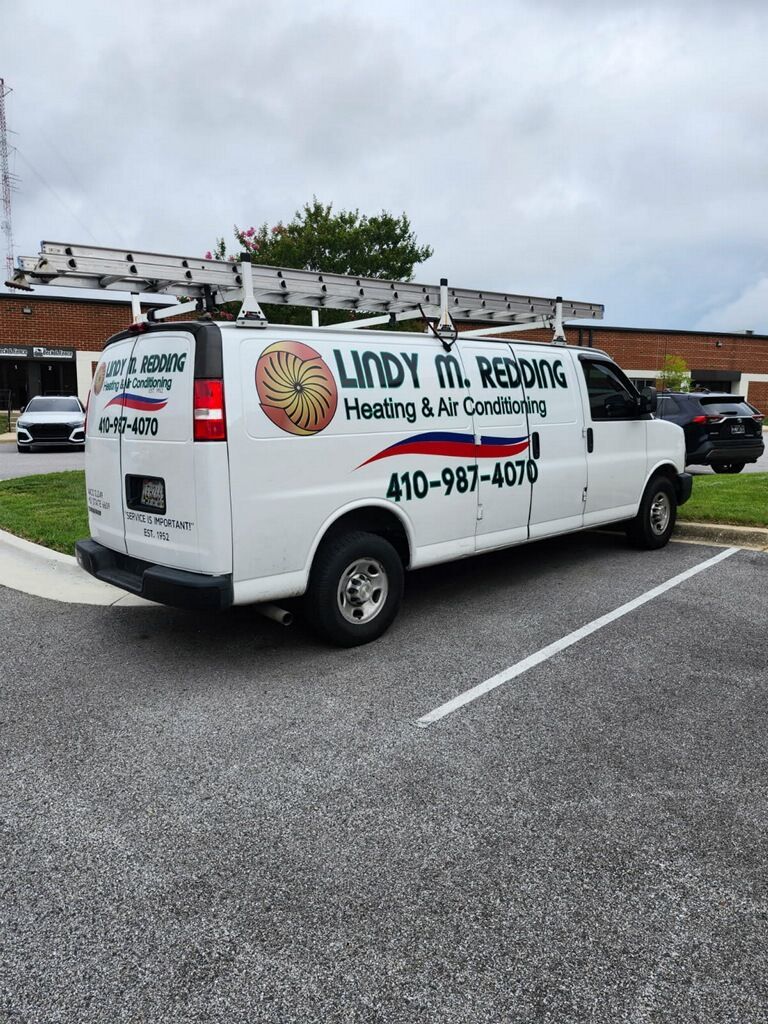White utility van with ladder racks and company logo parked in a lot under cloudy skies.