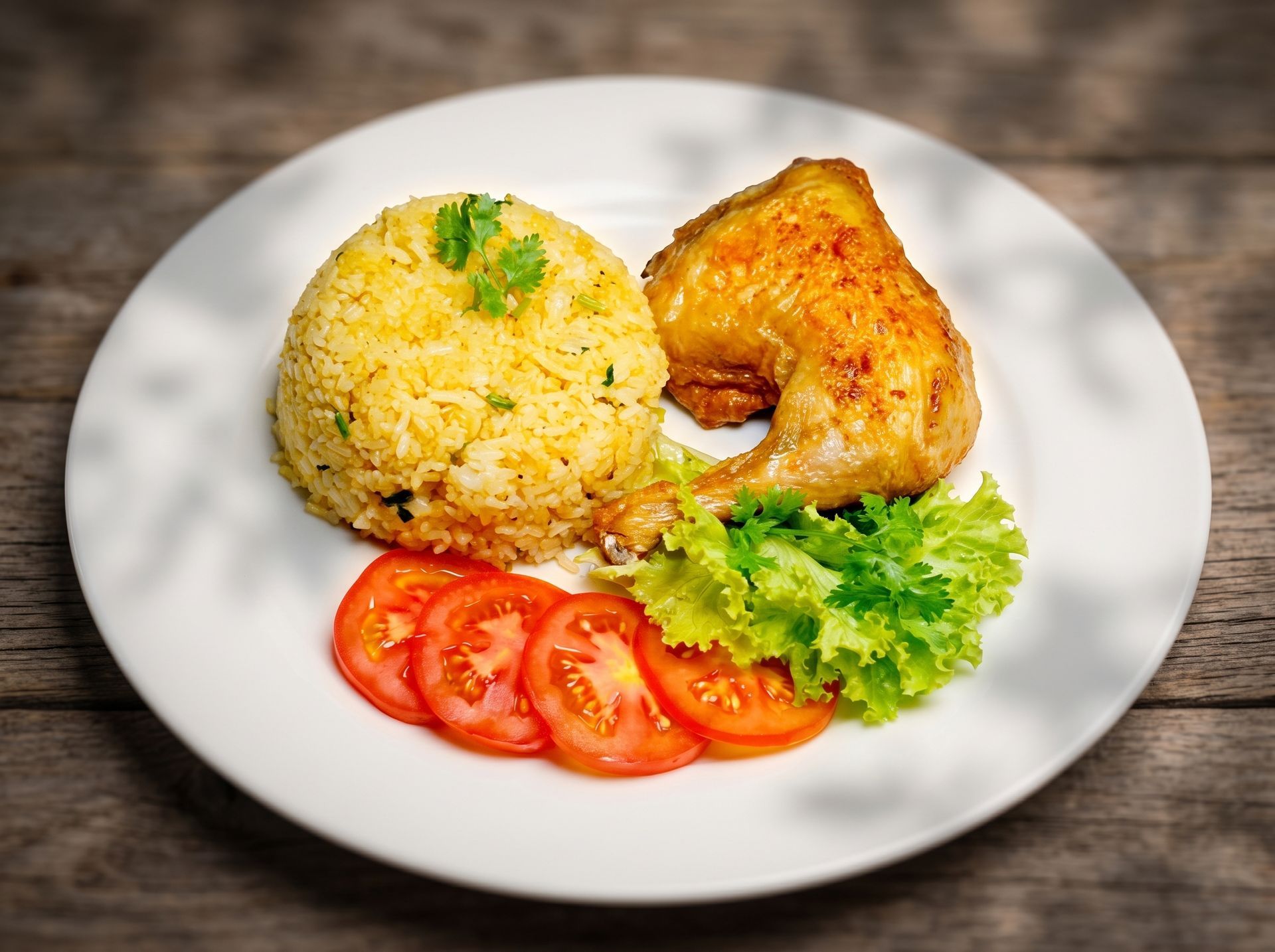 Rice, roasted chicken, tomato slices, and lettuce on a white plate