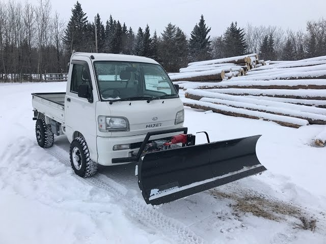 Person using a snowblower, spraying snow on a sunny winter day.