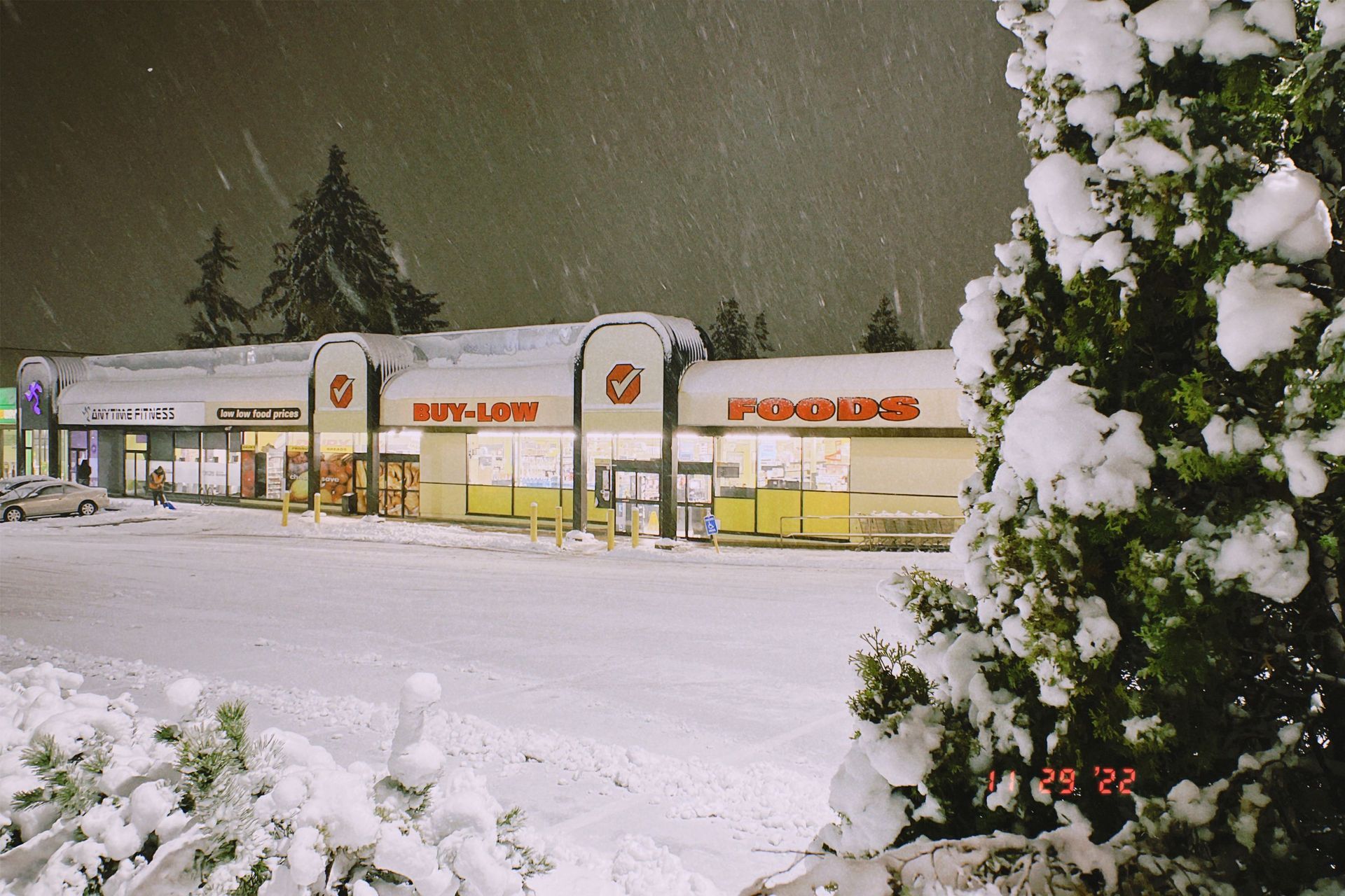 Snowy parking lot outside a row of lit stores at night