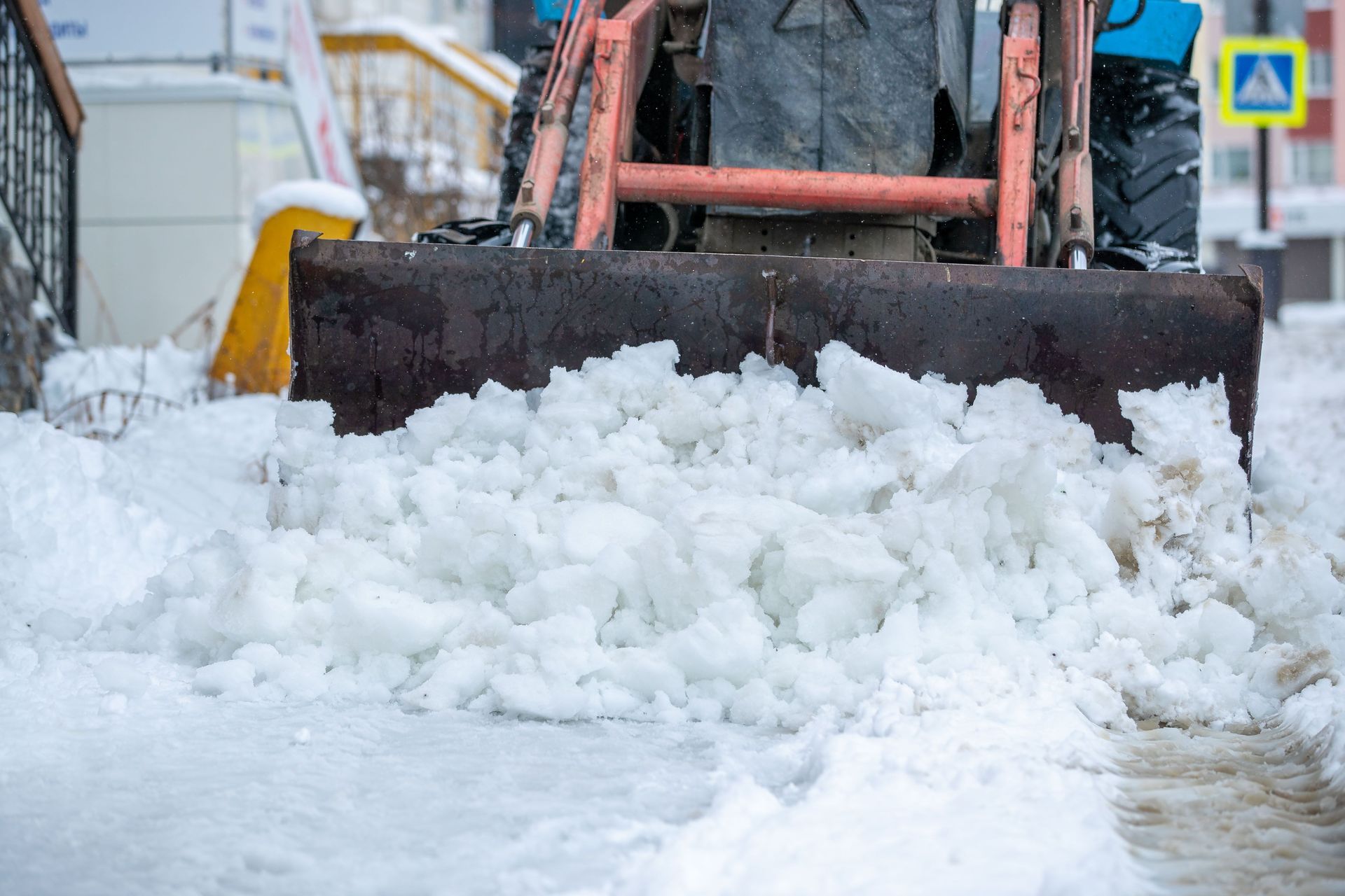 Snowplow clearing thick snow from a street, with a pedestrian crossing sign in the background