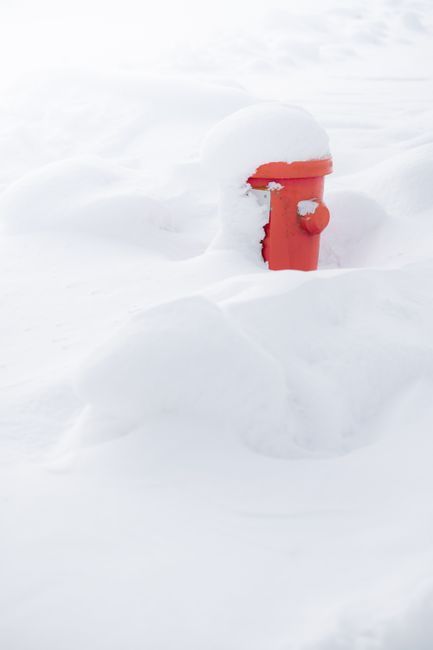 Red fire hydrant half-buried in deep snow on a white, snowy landscape