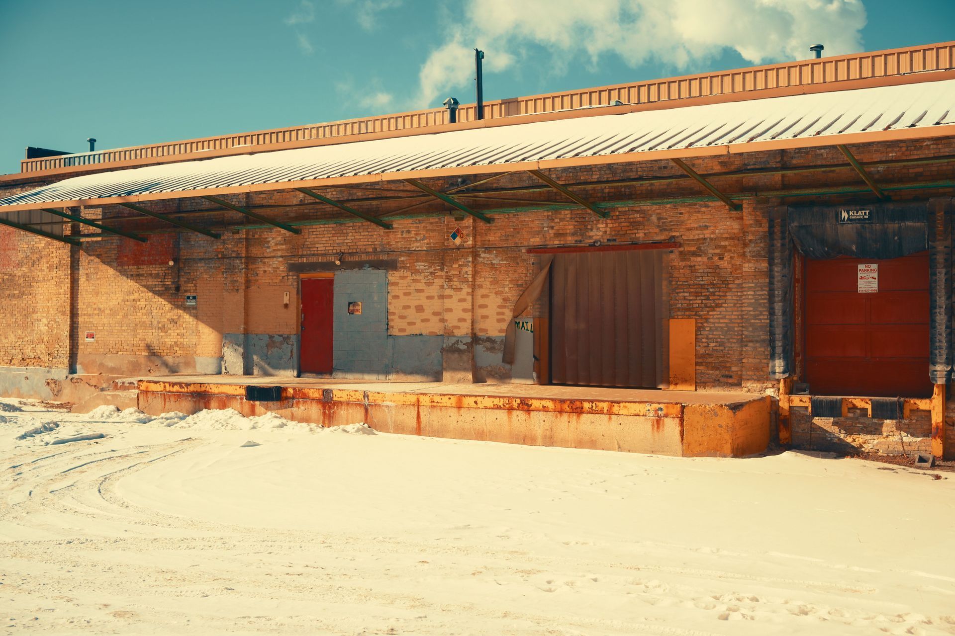 Brick building with red doors and windows in a snowy, sunlit landscape