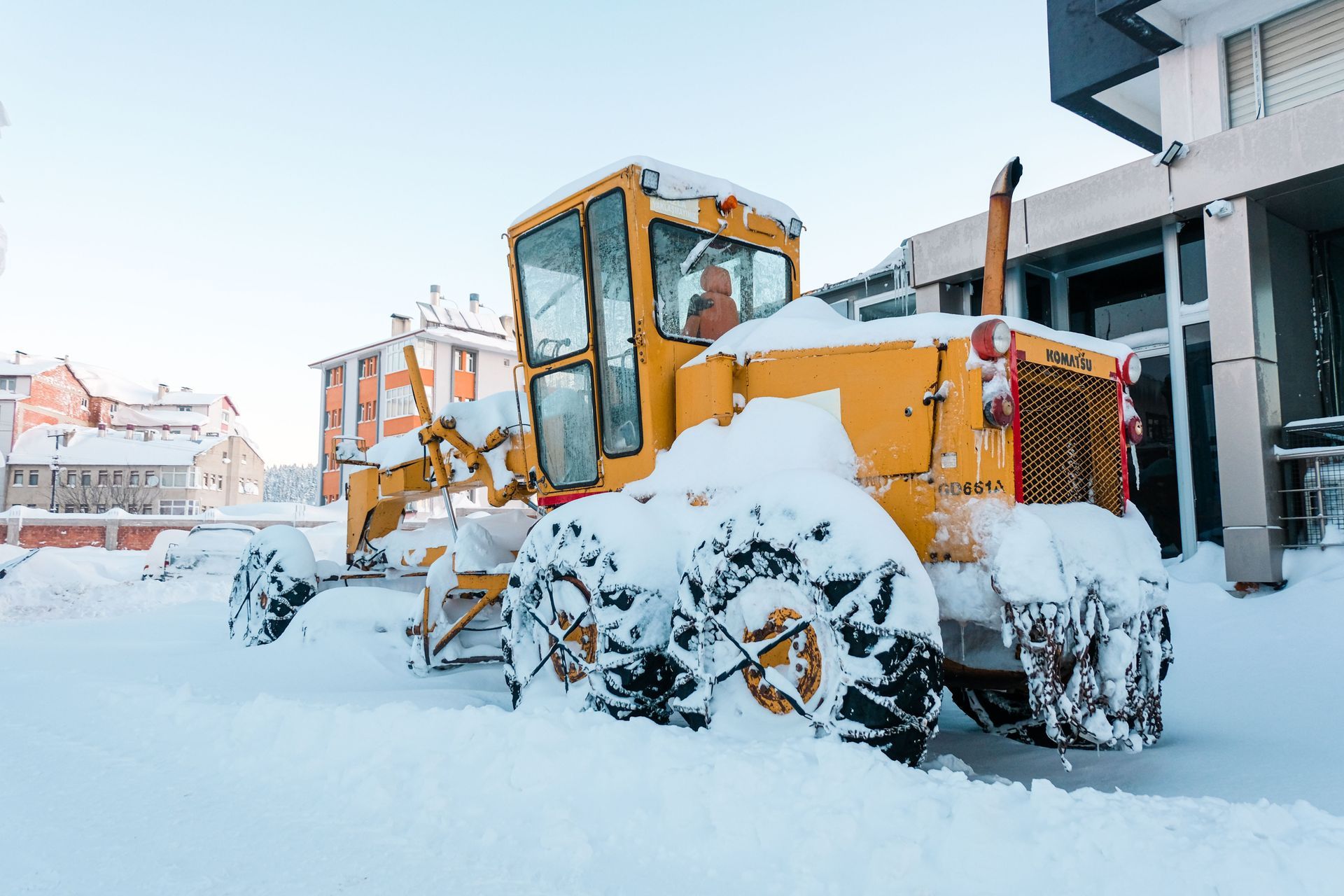 Yellow snowplow clearing deep snow on a street beside buildings