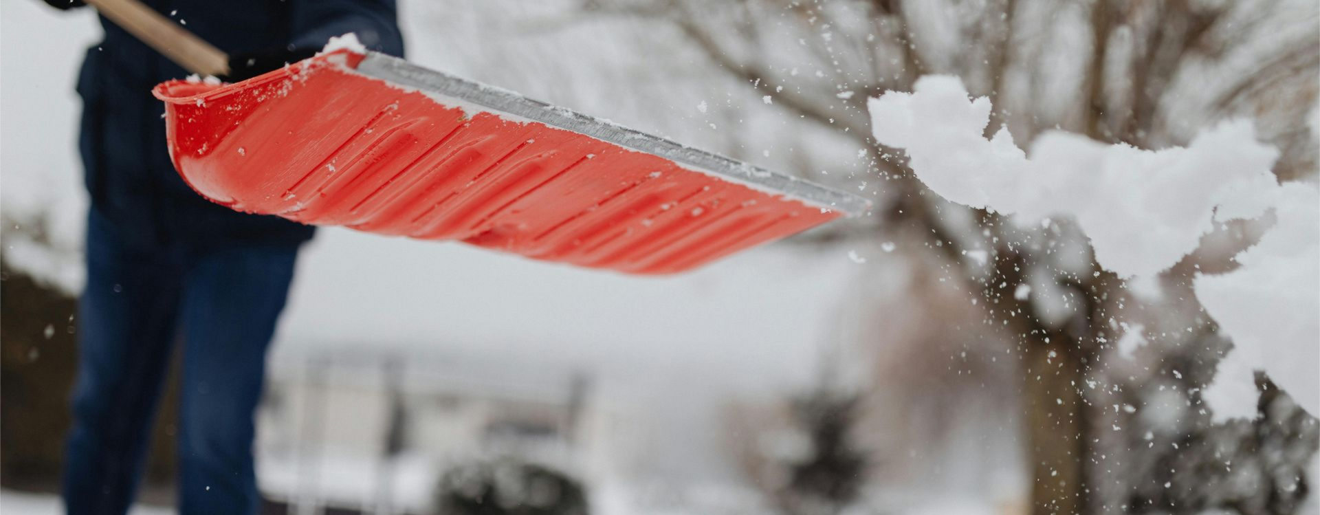 Person shoveling snow with a red shovel on a snowy day.