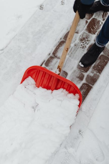 Person shoveling snow from a brick pathway with a red shovel.