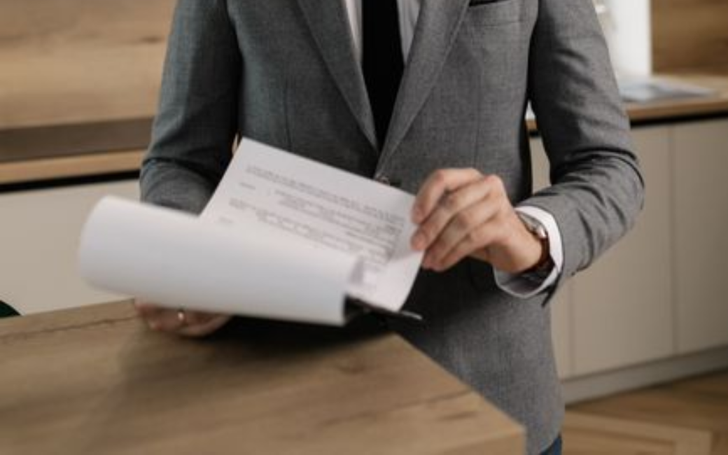 Person in a gray suit flipping through papers at a desk in a modern office kitchen