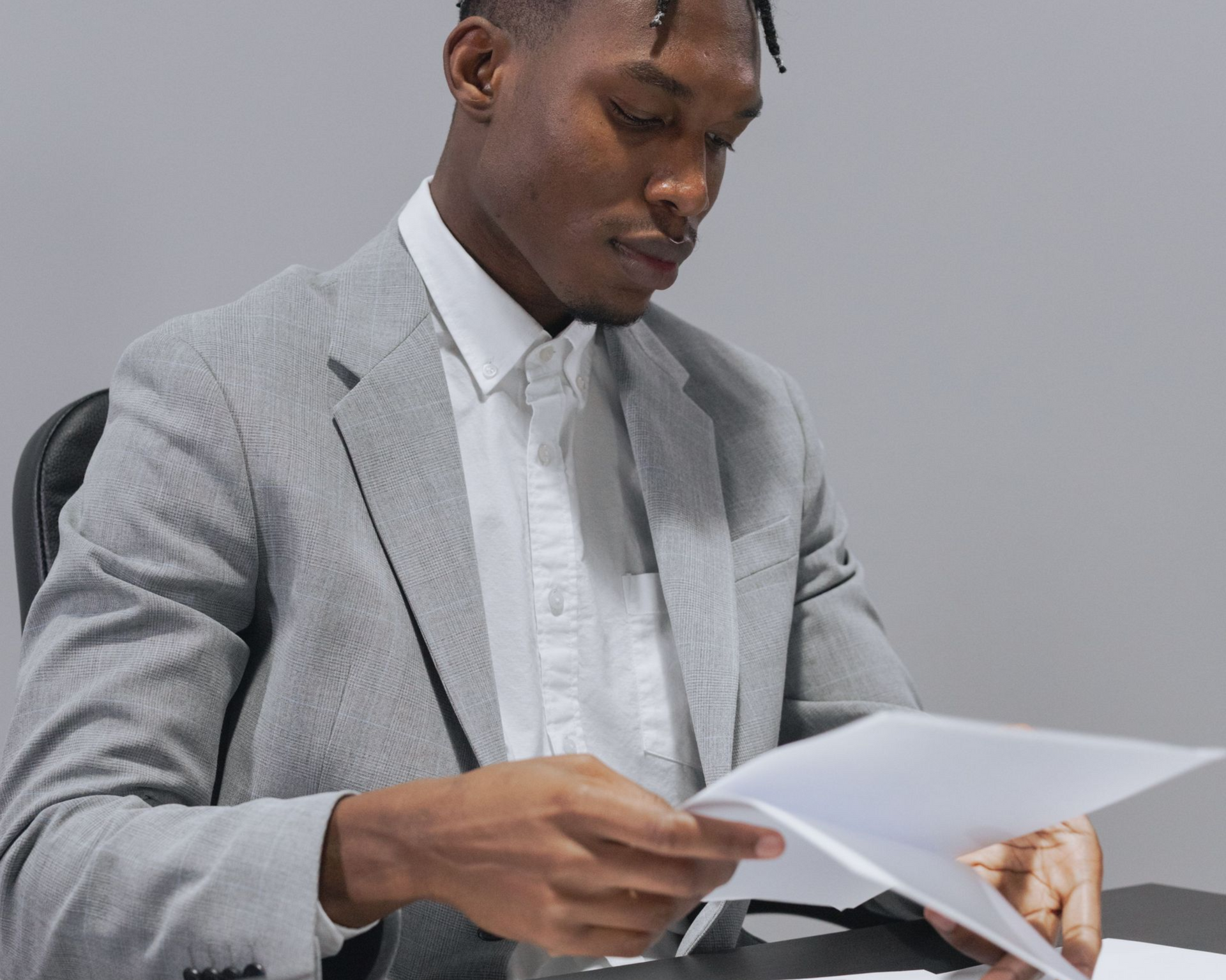 Man in a light gray suit reviewing papers at a desk in a minimalist office