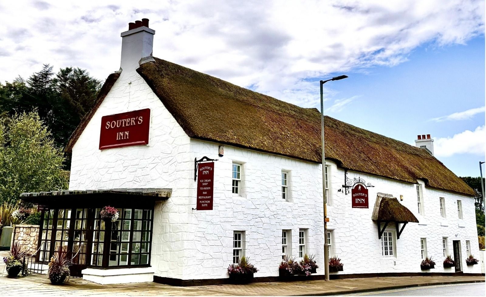 an image showing a white thatched pub building with red signs reading Souter's Inn and a glass-front entrance on a street corner. 