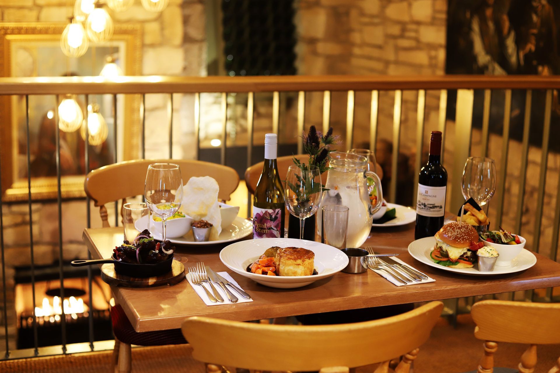 an image showing an elegant dinner table set with plates of food, wine bottles, and candles in a warm indoor setting
